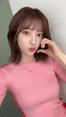 a woman wearing a pink sweater and a necklace is taking a selfie