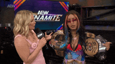 two women are standing in front of a aew dynamite screen