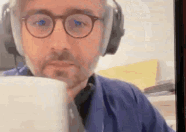 a man wearing glasses and headphones is drinking from a mug .