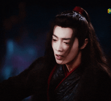 a man with long black hair and a red ribbon in his hair looks at something