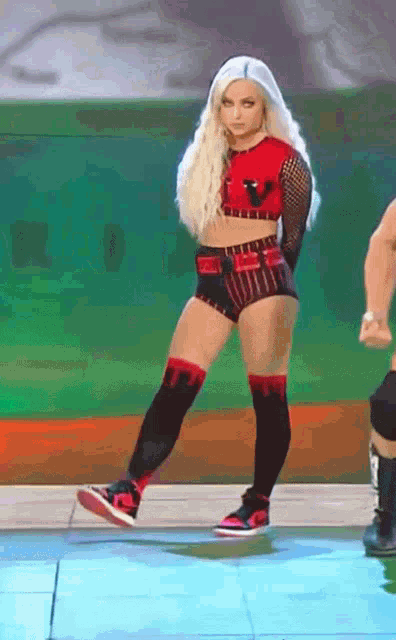 a blonde woman in a red top and black shorts is dancing on a stage .