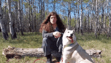 a man with long hair sits on a log with a dog