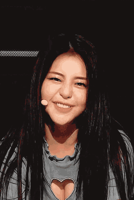 a woman with long hair is smiling and wearing a heart shaped cut out shirt