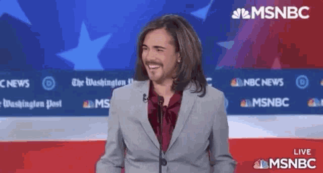 a man in a suit and tie is standing in front of a microphone and smiling .
