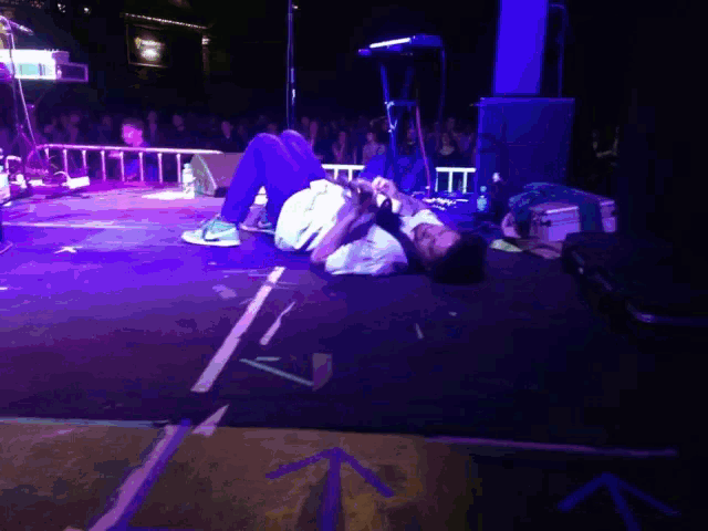 a man is laying on the floor playing a guitar in front of a crowd