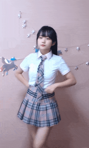 a girl in a school uniform and tie is dancing in front of a wall with unicorns on it .