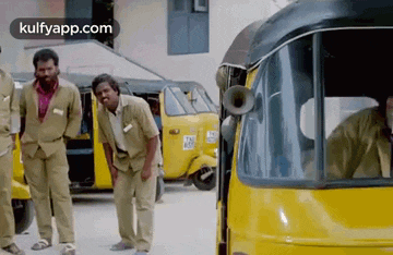 a group of men are standing in front of a yellow auto rickshaw with a horn .