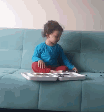 a little girl is sitting on a blue couch playing with a tray
