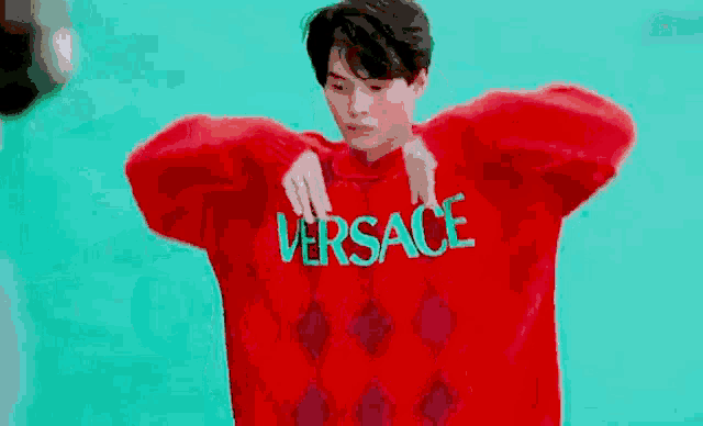 a young man is wearing a red sweater with the word versace embroidered on it .
