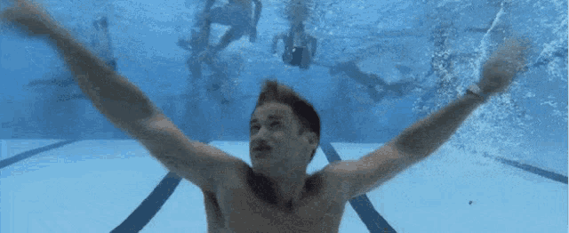 a shirtless man is swimming underwater in a pool with his arms outstretched .