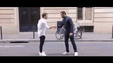 two men are shaking hands on a city street .