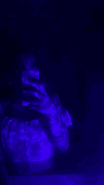a person is taking a picture of themselves with a cell phone in a dark room with a blue light behind them .