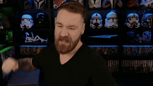 a man with a beard is flexing his muscles in front of a shelf full of storm trooper helmets