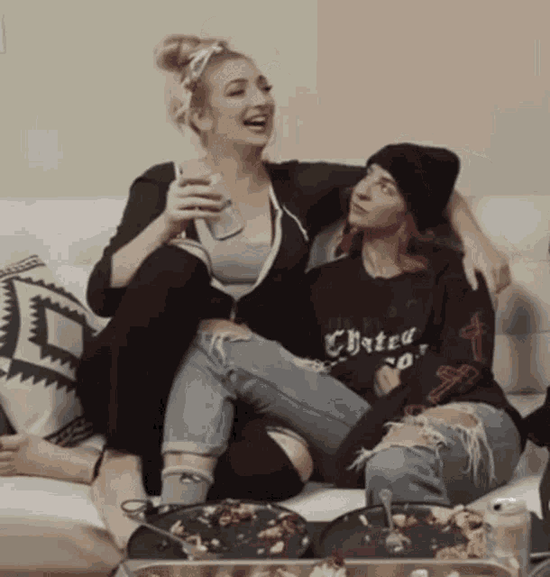 two women are sitting on a couch with one wearing a shirt that says hate on it .