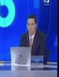 a man in a suit and tie is sitting at a desk in front of a computer monitor .