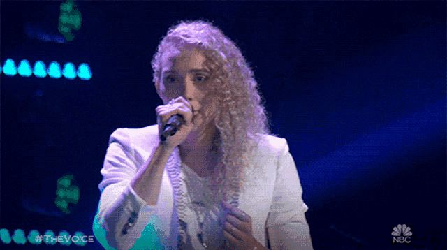 a woman singing into a microphone with nbc written on the bottom