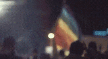 a crowd of people are holding a rainbow flag in the dark .