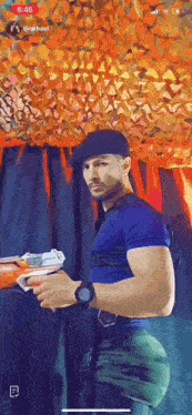 a man in a blue shirt and black hat is holding a nerf gun in his hand