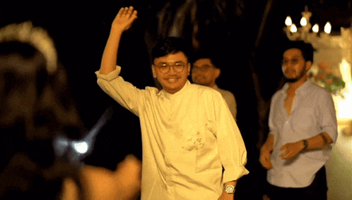 a man wearing glasses and a watch is waving