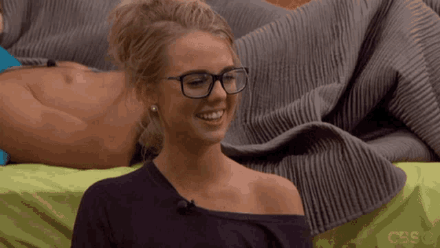 a woman wearing glasses is smiling in front of a man on a bed
