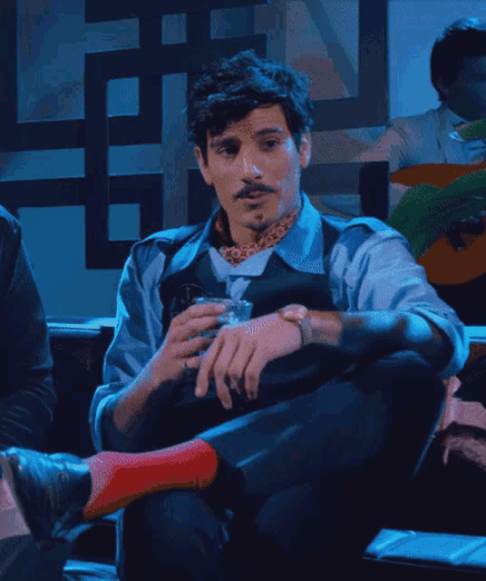 a man with a mustache sits in a chair holding a glass of wine