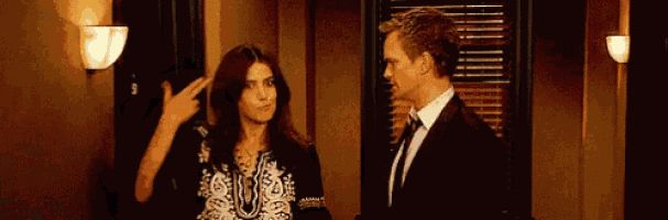 a man and a woman are standing next to each other in a room and the woman is pointing at the man 's head .