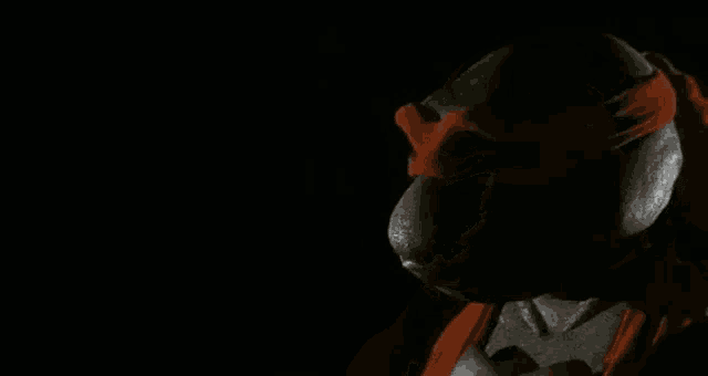 a close up of a teenage mutant ninja turtle in the dark with a red headband .