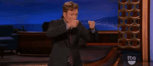 a man in a suit and tie is dancing on a stage with a tbs logo in the background