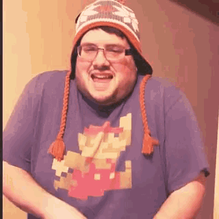 a man wearing a hat and glasses is wearing a shirt with a pixelated mario on it