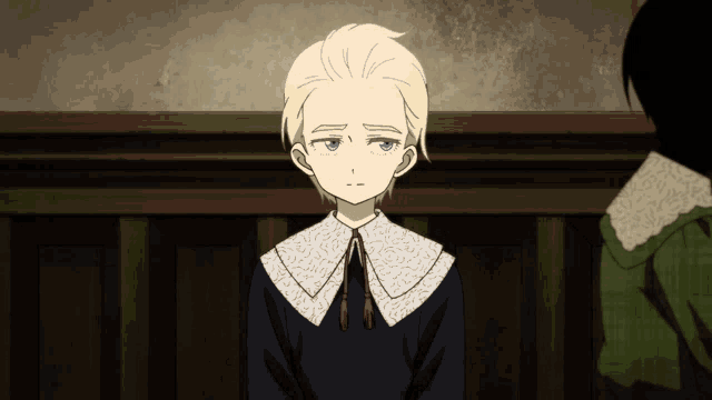 a boy with blonde hair and a white collar is sitting in a dark room