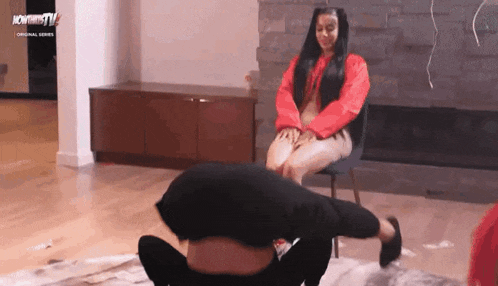 a woman in a red sweater is sitting on a chair next to a man doing a handstand .