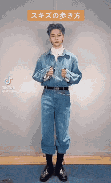 a man in a blue jumpsuit is standing in front of a wall holding a pair of scissors in his hands .