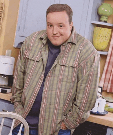 a man in a plaid shirt is smiling in a kitchen