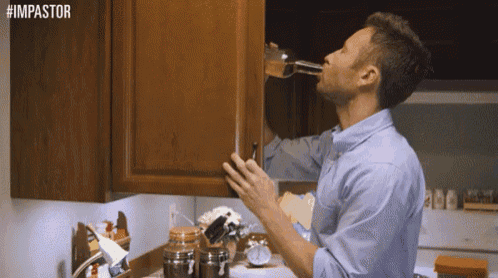 a man in a blue shirt is drinking from a glass in a kitchen