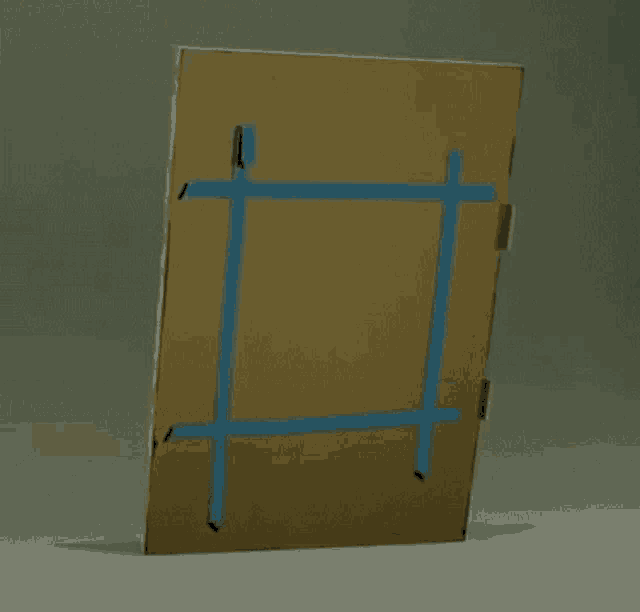 a cardboard box is taped to a gray surface with blue tape