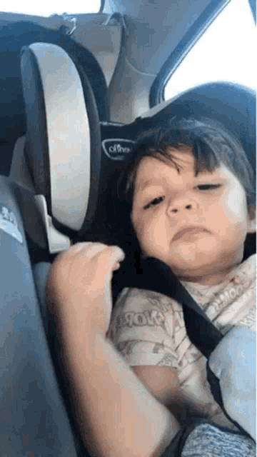 a little boy is sitting in a car seat with a sad look on his face .