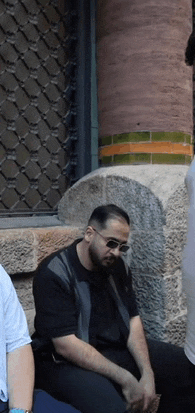 a man wearing sunglasses sits in front of a brick wall