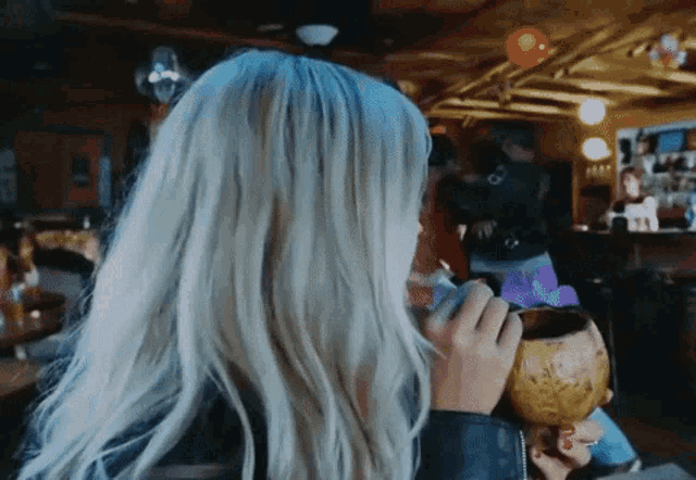 a woman with long blonde hair holds a coconut in her hand