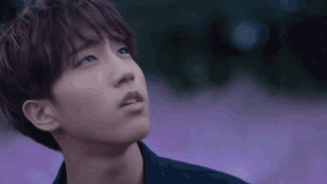 a young man with a purple background is looking up at the sky .