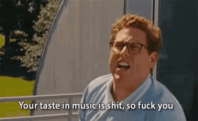 a man wearing glasses is making a funny face and saying `` your taste in music is shit , so fuck you `` .