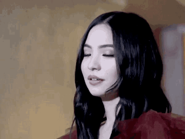 a woman with long black hair is wearing a red dress and looking at the camera with her eyes closed .