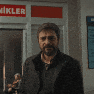 a man with a beard is standing in front of a sign that says " ikler "