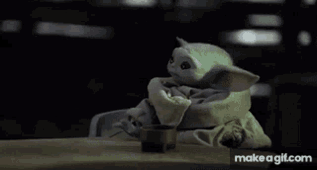 a baby yoda doll is sitting at a table with a cup of coffee .