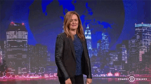 a woman stands in front of a city skyline and waves her hand in front of a comedy central logo