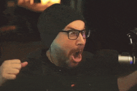 a man wearing glasses and a beanie is making a funny face while talking into a microphone .