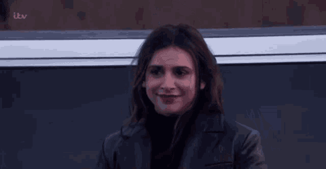 a woman wearing a black jacket and a black turtleneck is smiling .