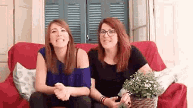 two women are sitting on a red couch talking to each other and smiling .