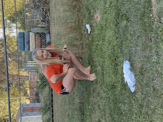 a woman in a red shirt is squatting in the grass