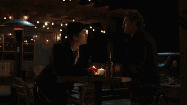 two men are sitting at a table with a bottle of beer and candles