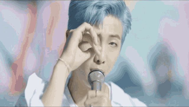 a man with blue hair is holding a microphone and making a heart with his hands .